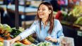 Stunning smiling brunette standing at farmers market and choosing vegetables for healthy meal.